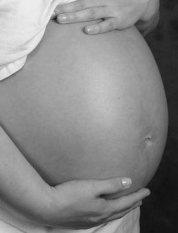 A black and white close-up of a pregnant woman's belly, with her hands cradling it.