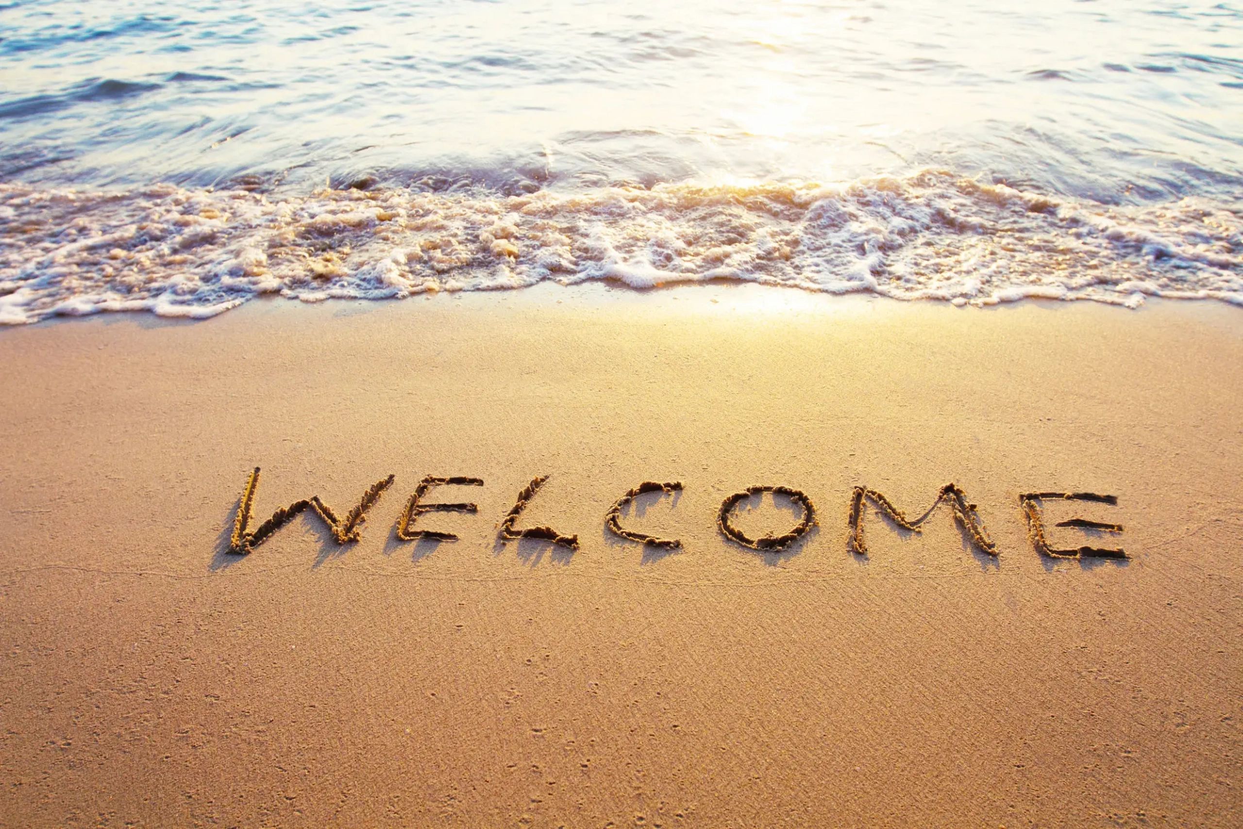 The word "WELCOME" is written in the sand near the ocean shore.