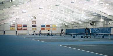 Indoor tennis courts with bright lighting and banners on the walls.