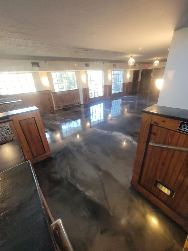 Metallic reflective epoxy floor in a spacious room with wooden accents and large windows.