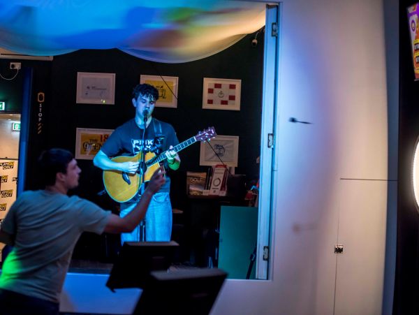 Man playing guitar and singing while another plays darts.