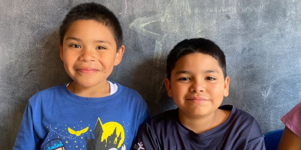 Two boys smiling in front of a chalkboard wall.