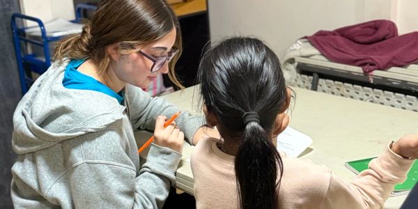 A woman helps a young girl with her homework at a table.