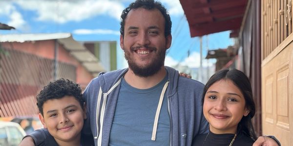 A smiling man with two children outdoors on a sunny day.
