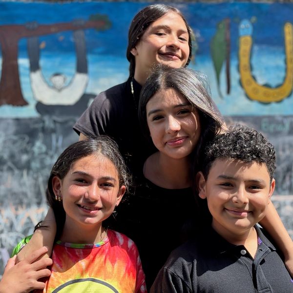 Four smiling young friends posing closely outdoors on a sunny day.