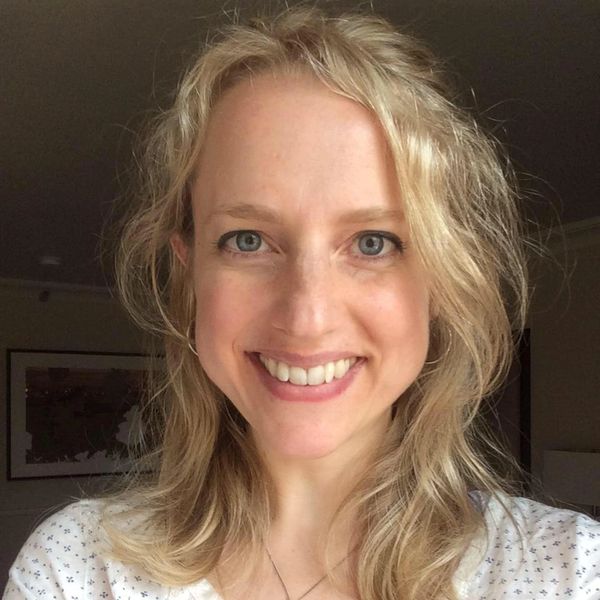 Smiling woman with curly blonde hair in a softly lit room.