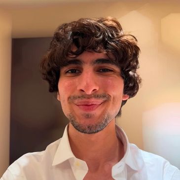 Young man with curly hair smiling in a white shirt.