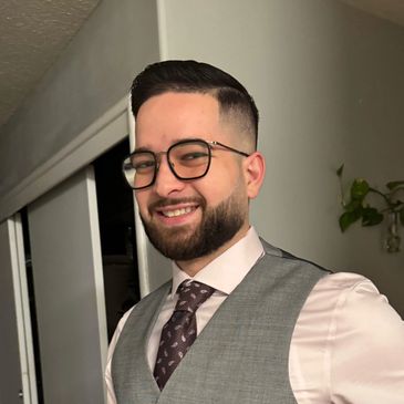Smiling man wearing glasses, a tie, and a vest indoors.