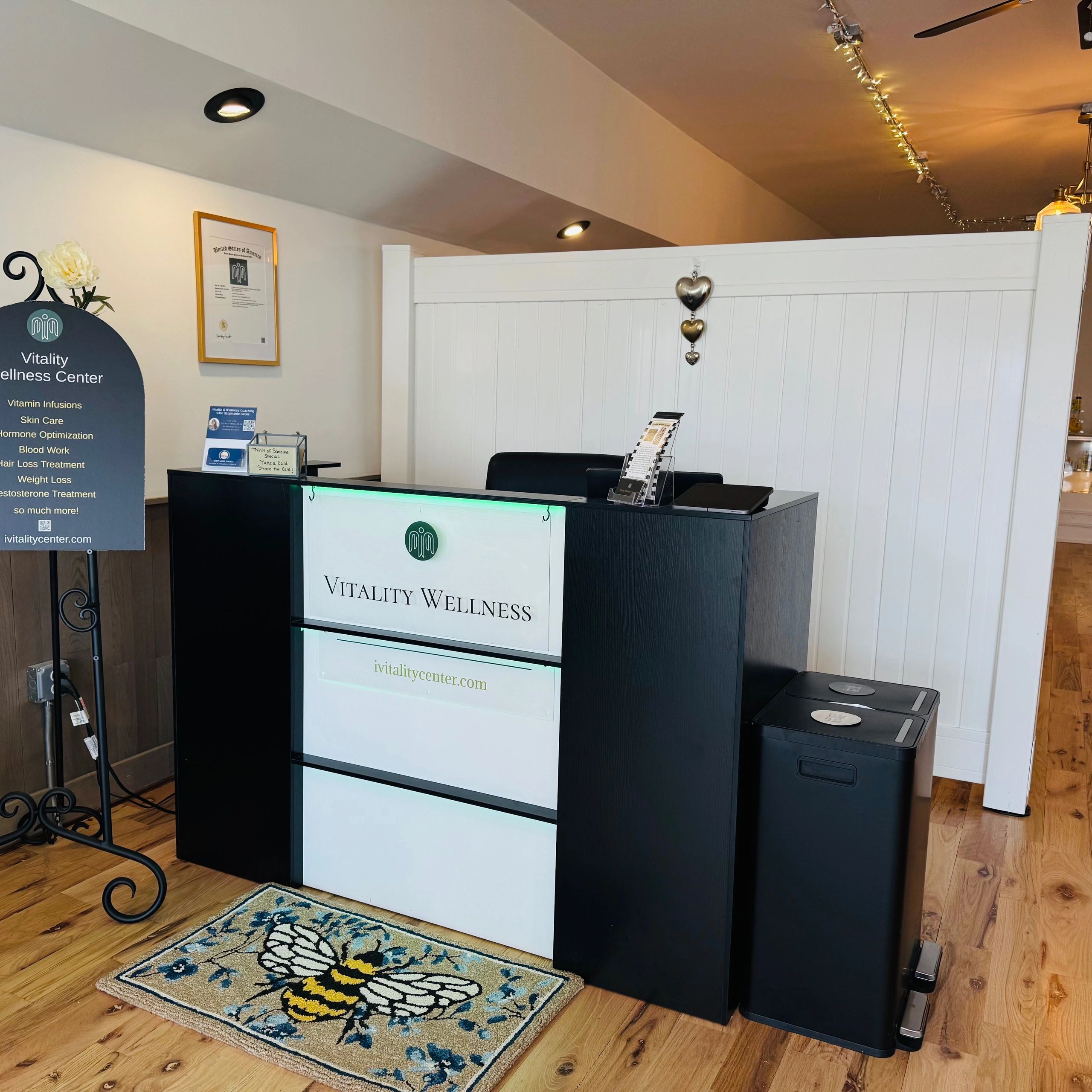 Front desk of Vitality Wellness Center with a bee-themed rug and informational signage.