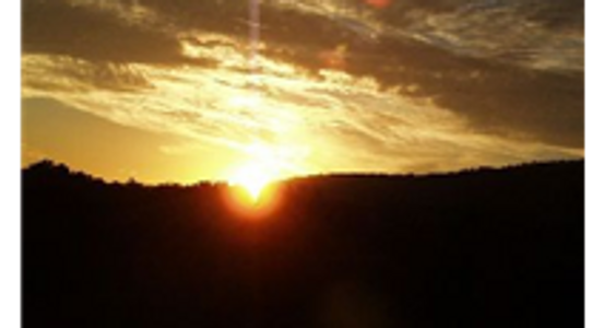Sunset behind a dark hill under a cloudy sky.
