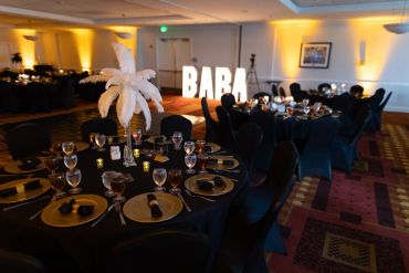 Elegant event tables with feather centerpieces and glowing "BARA" sign.