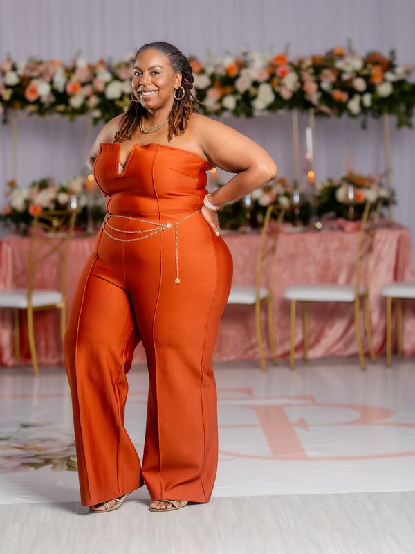 Woman in an elegant orange jumpsuit smiling at a formal event.