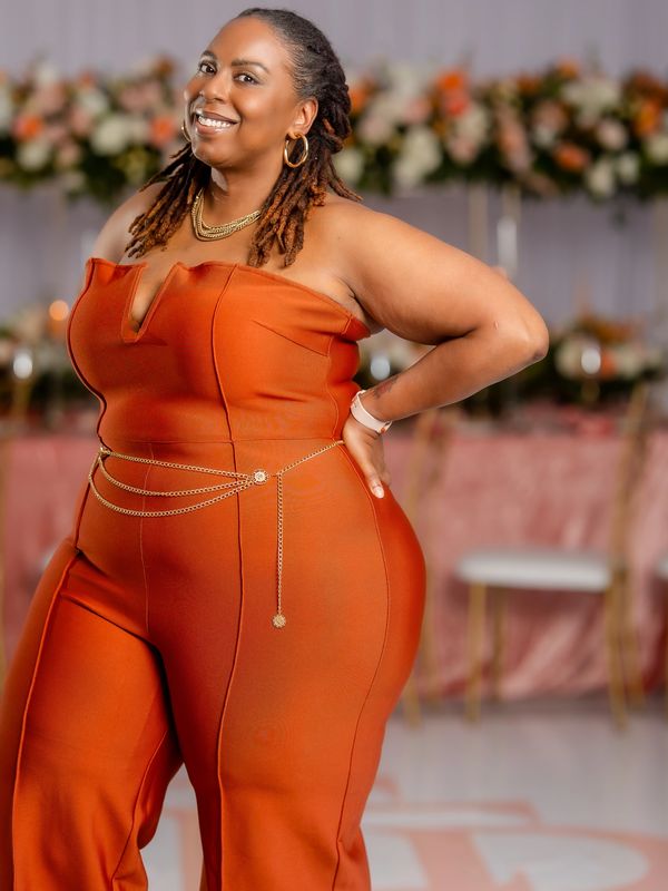 Woman smiling in an orange jumpsuit with gold accessories.