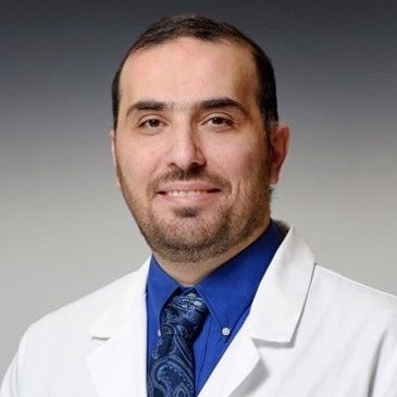 Man in a white medical coat and blue shirt with tie.