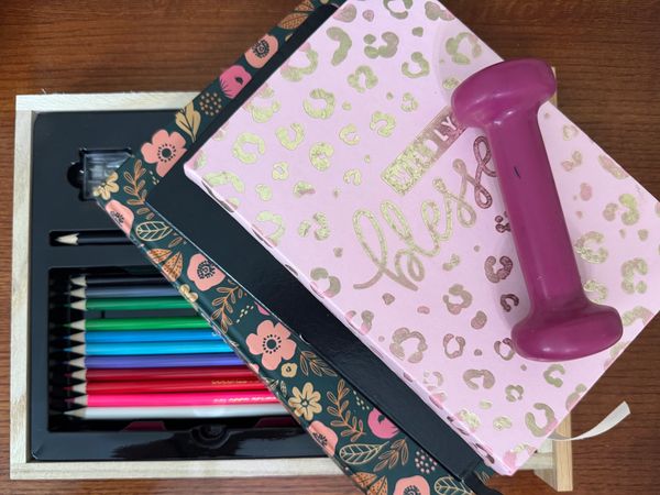 A pink dumbbell on top of floral and leopard-print notebooks with colored pencils.