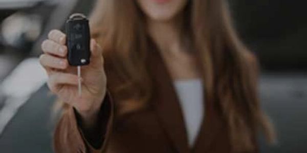 Happy woman holding car keys in focus with blurred background.