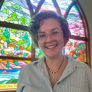 Smiling person in glasses in front of colorful stained glass.