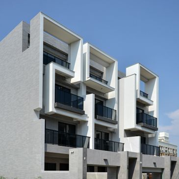 Modern white building with geometric balconies and black railings under clear blue sky.