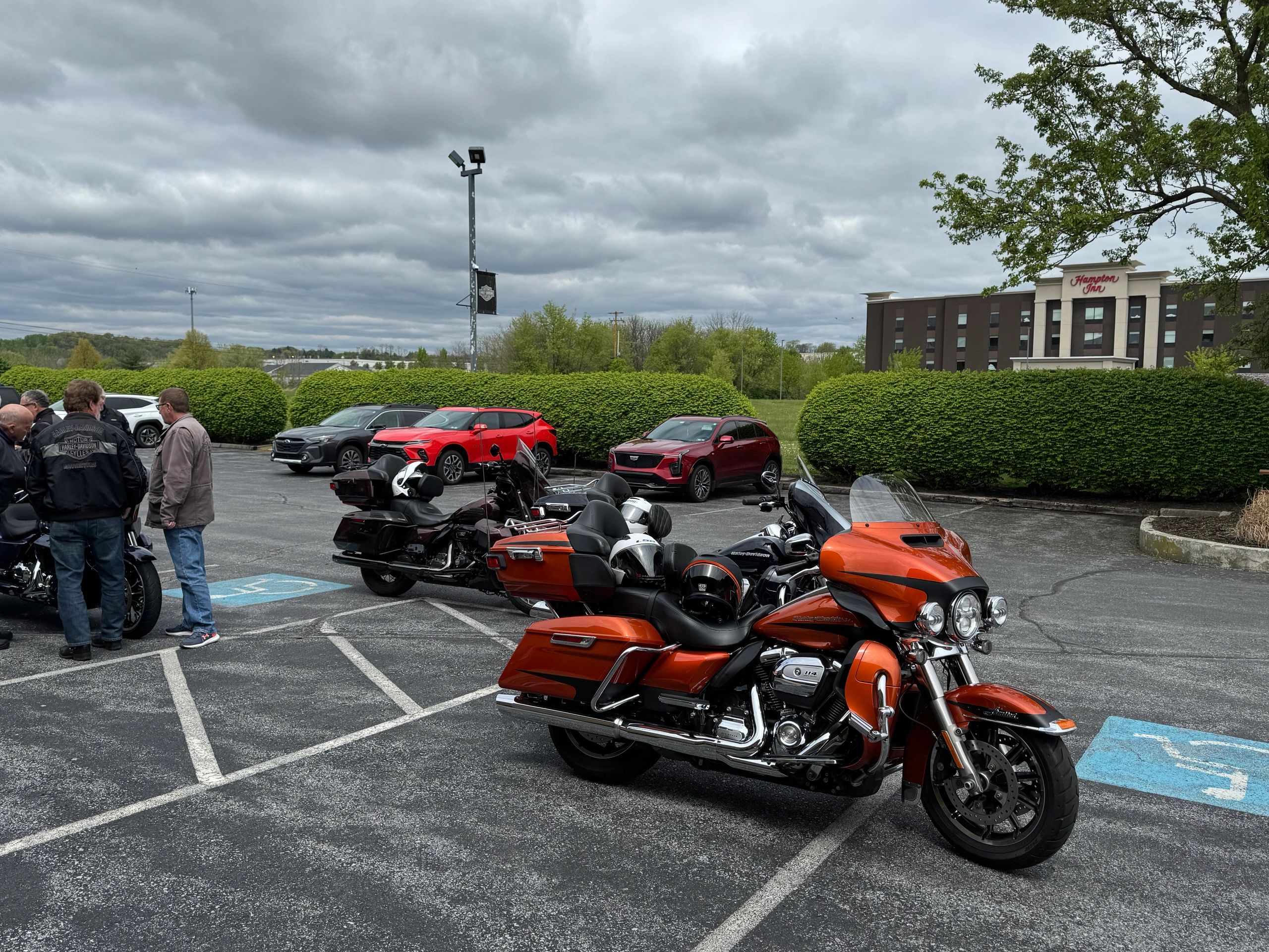 Group of motorcycles and people gathered in a parking lot near Hampton Inn on a cloudy day.