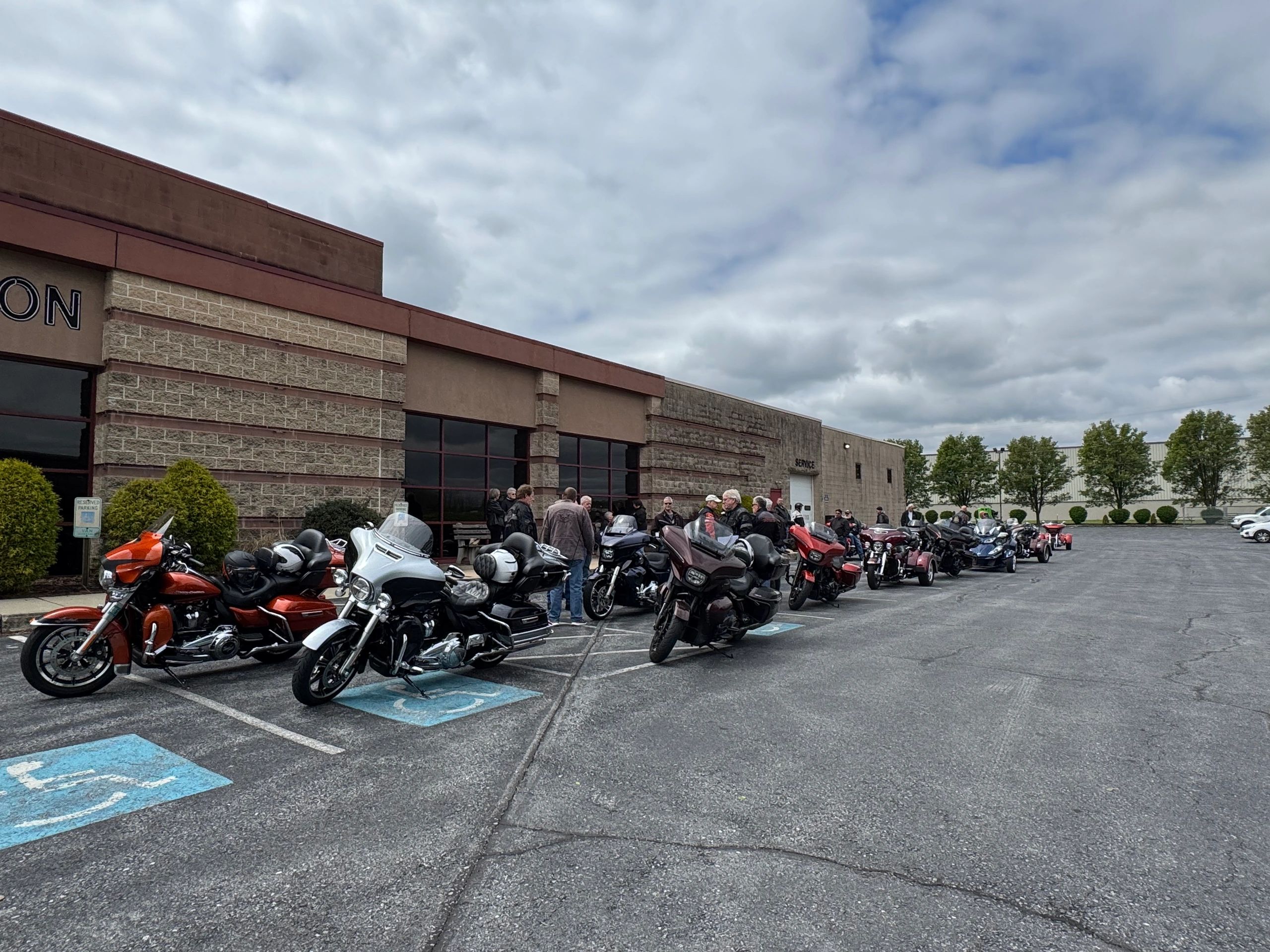 Motorcycle enthusiasts gathered outside a building under a cloudy sky.
