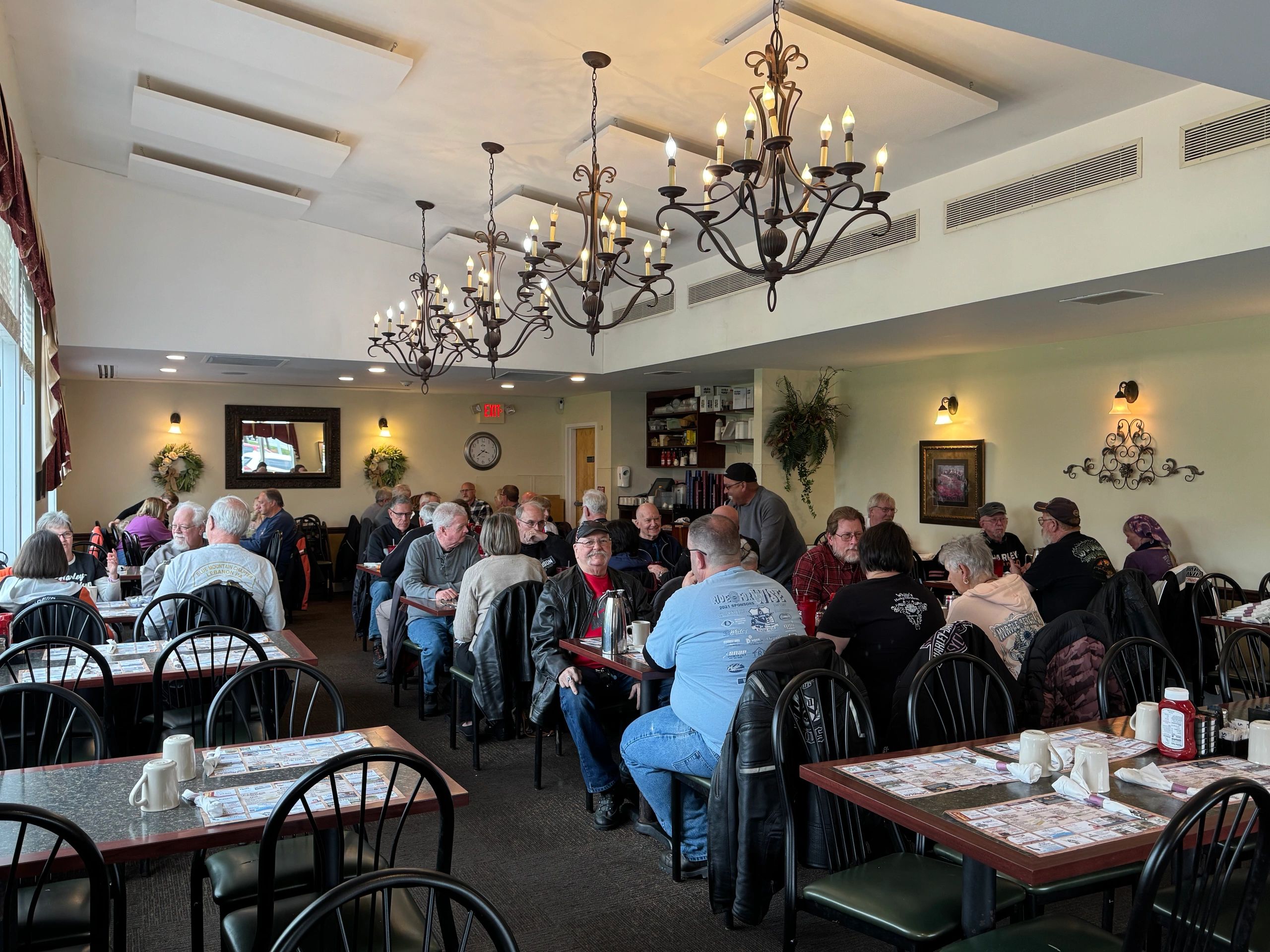 Busy dining room filled with people enjoying a meal under elegant chandeliers.