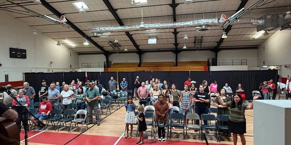 Community gathering in a gymnasium with people standing and listening.