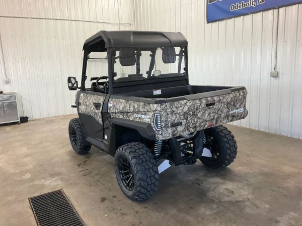 Camouflaged utility terrain vehicle parked inside a garage with large wheels.