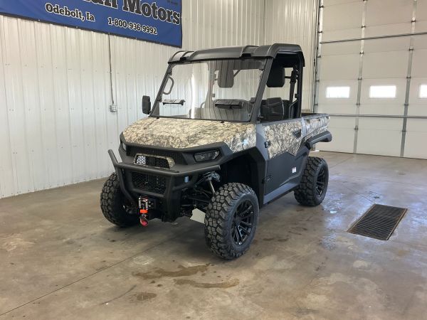 Camouflaged utility terrain vehicle parked indoors with large off-road tires.