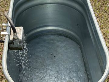 Water flowing into a large metal tub outdoors.