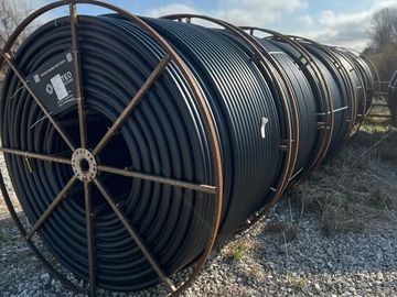 Large industrial spools holding coiled black tubing outdoors.