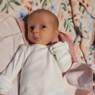 Newborn baby lying on a floral blanket, wearing a white outfit.