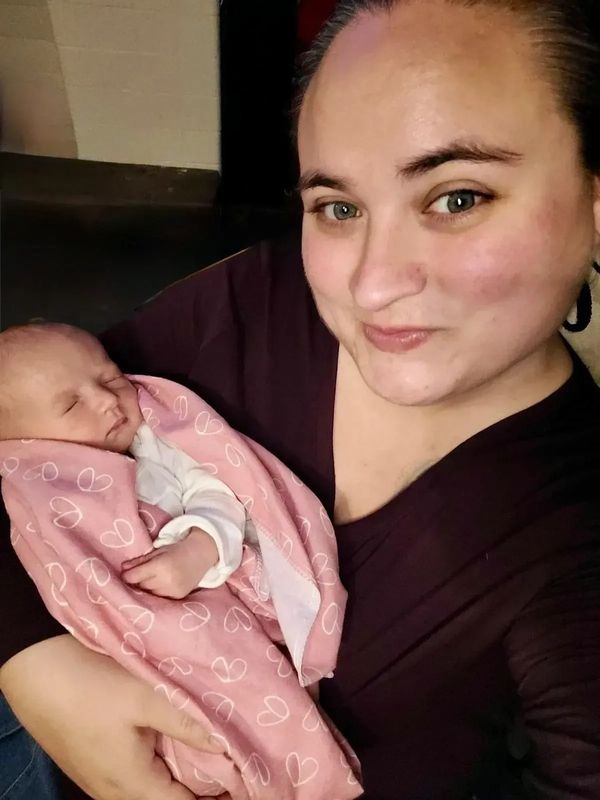 A woman smiling while holding a sleeping baby wrapped in a pink blanket.