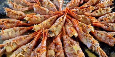 Shrimp arranged in a circular pattern cooking with butter in a pan.