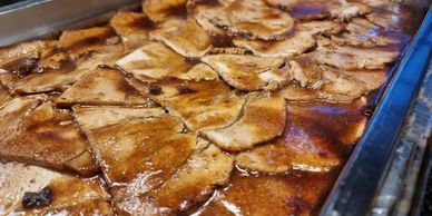 Close-up of cooked meat slices in rich brown sauce in a metal tray.