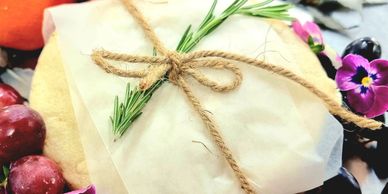 Wrapped package with twine and rosemary, surrounded by fruits and flowers.
