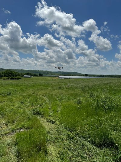 A drone flying over a green field under a partly cloudy sky.