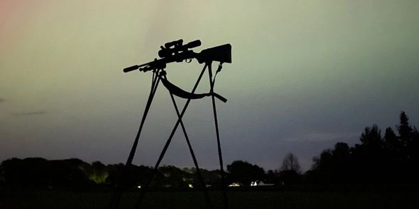 Silhouette of a sniper rifle on a stand at dusk.