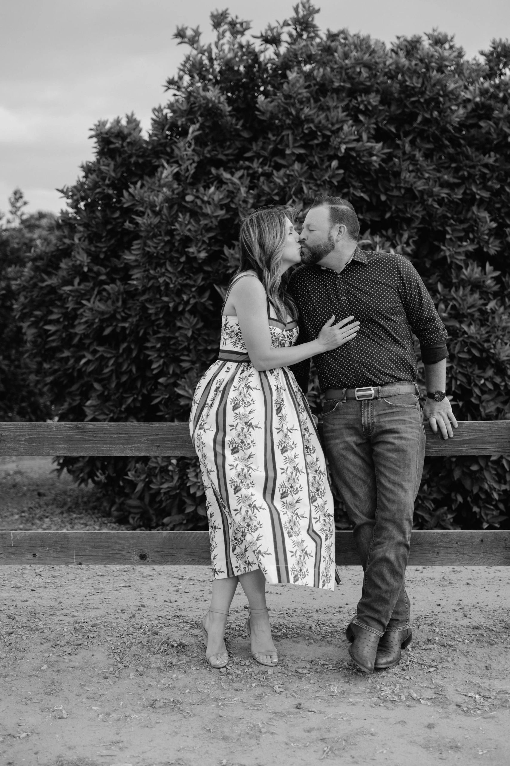 Lizy and Chris sharing a kiss by a wooden fence