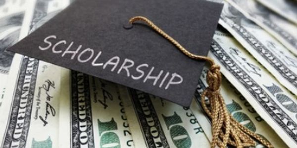 Graduation cap labeled 'Scholarship' resting on hundred-dollar bills.