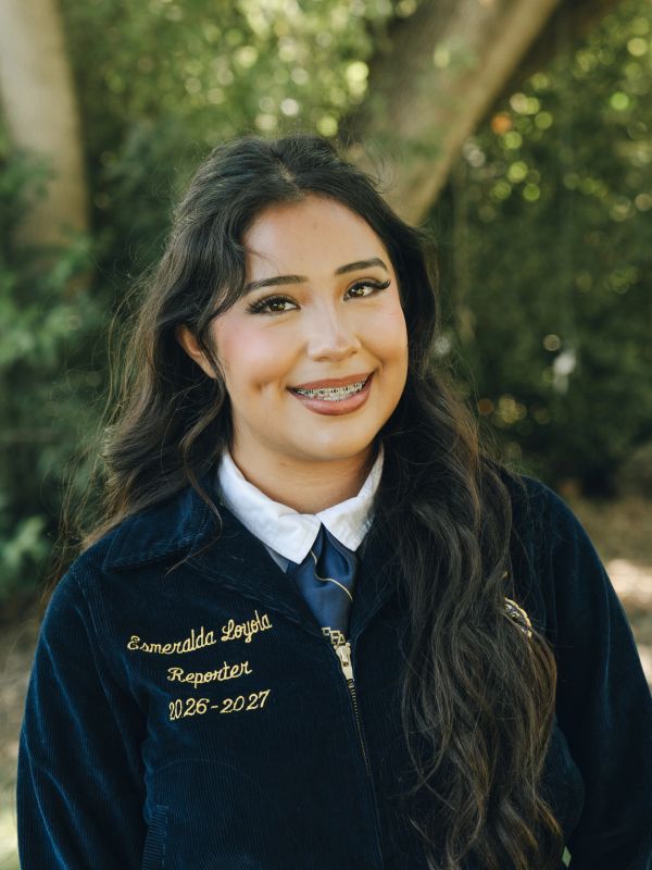 Young woman smiling outdoors in a formal jacket.