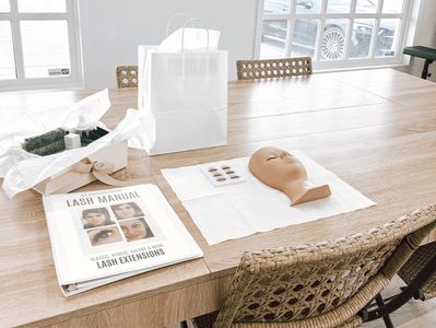 Lash extension training setup on a desk with a mannequin head and manual.
