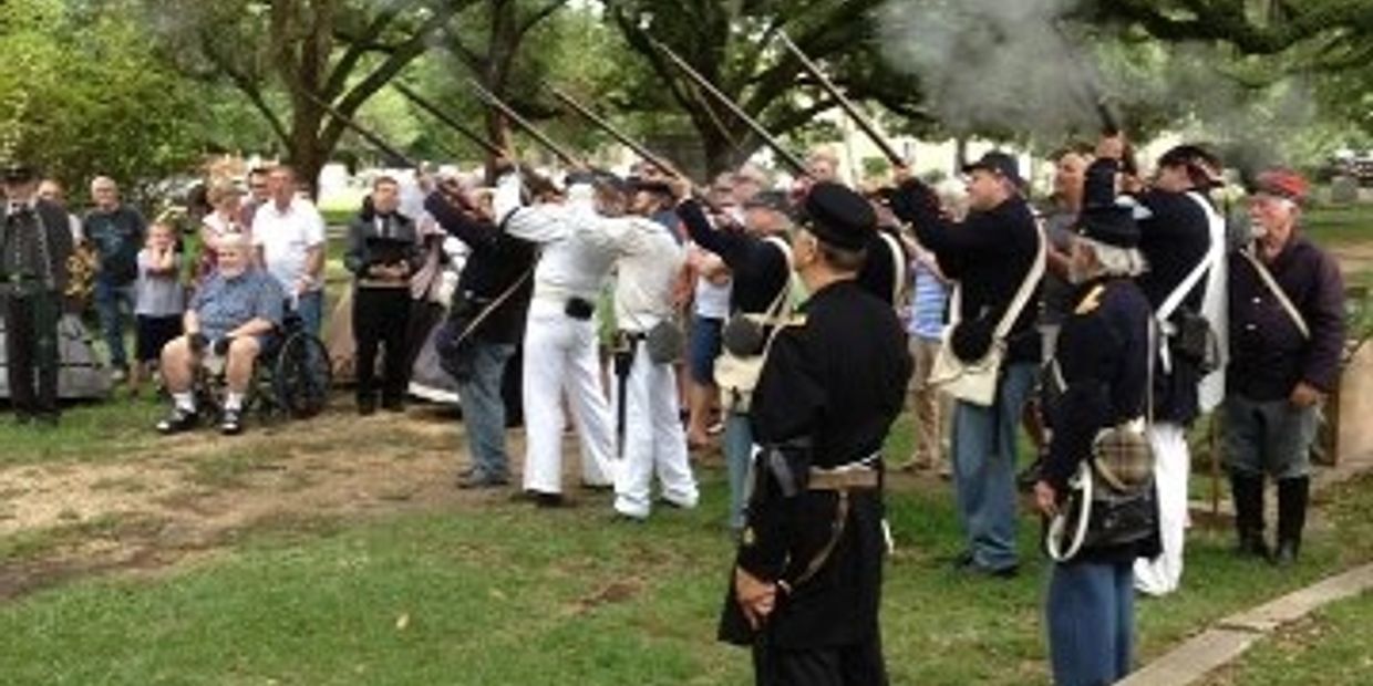 Civil War reenactors performing a rifle salute in a park with an audience.