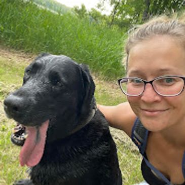Smiling woman with black dog outdoors.