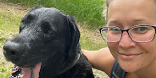 Smiling woman with black dog outdoors.