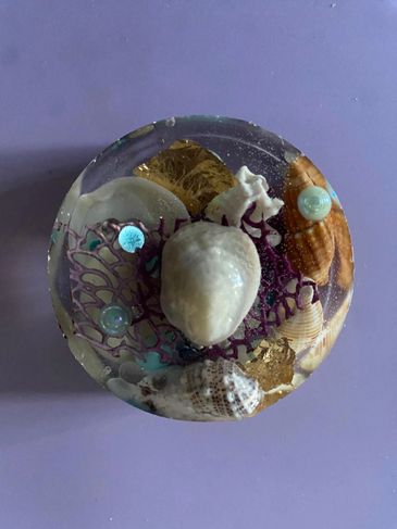 Decorative resin piece with embedded seashells and pearls on a purple background.