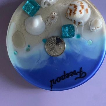 Decorative plate with seashells, blue resin, and a coin.
