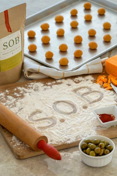 S.O.B. bag with dough-covered olives on baking sheet and flour dusted with S.O.B. logo on counter