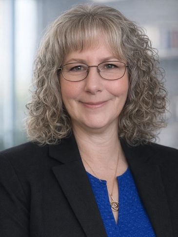 Professional woman with curly hair wearing glasses and a blazer.