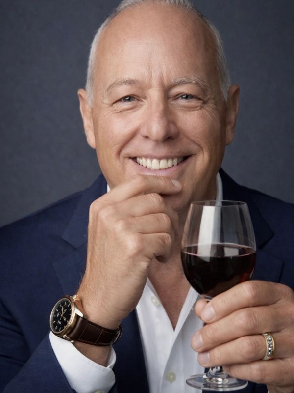 Smiling man in a suit holding a glass of red wine.