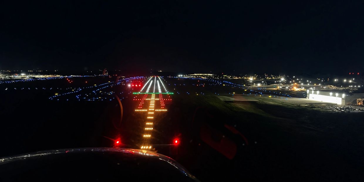 Nighttime runway illuminated with colorful landing lights and airport lights in the distance.